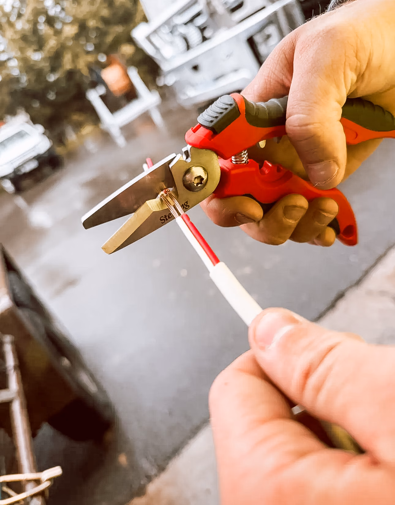 Close-up of hands cutting a copper wire with red-handled wire stripper.